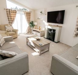 A living room with two grey sofas a beige armchair a coffee table a TV mounted above a fireplace and windows with plaid curtains at Rockpool Retreat in Runswick Bay near Hinderwell
