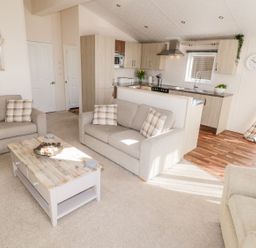 A living room with beige sofas and a wooden coffee table next to a kitchen with wooden cabinets at Rockpool Retreat in Runswick Bay near Hinderwell