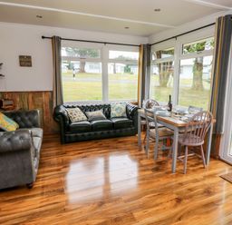 A sitting area with two sofas and a dining table with chairs next to large windows at Ty Haf in Roch