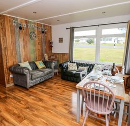 A living room with two sofas a wooden dining table and large windows at Ty Haf in Roch