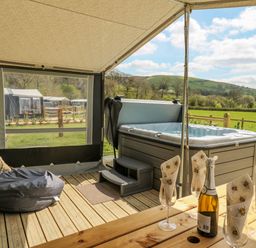 A covered outdoor decking area with a hot tub bean bag seating and a wooden table with glasses and a bottle at The Salmon in Nantmel near Rhayader