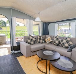 An enclosed seating area with a corner sofa and two round tables overlooking a deck with a hot tub at The Salmon in Nantmel near Rhayader