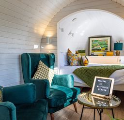 A room with two teal armchairs a small round glass table with a welcome sign and a bed with green quilt and colorful pillows at Veiko - Mayflower Meadow in Burshill near Brandesburton