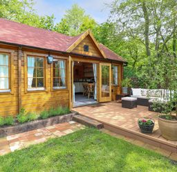 A wooden cabin with an open door leading to a deck with seating and plants at Willow Lodge in Potter Heigham