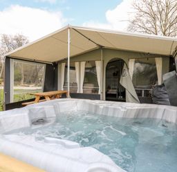 An outdoor hot tub in front of a large tent with picnic table and seating at The Otter in Nantmel near Rhayader