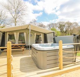 A wooden deck with hot tub and picnic table outside a tent in a wooded area at The Heron in Nantmel near Rhayader