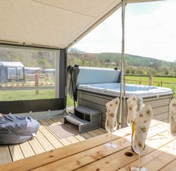 A covered outdoor area with a hot tub wooden table with glasses and napkins and a bean bag at The Heron in Nantmel near Rhayader