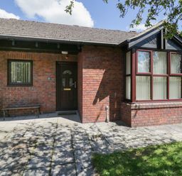 A brick house exterior with a dark front door, two windows, a bench, and a tiled patio at 21 Eamont Park Penrith