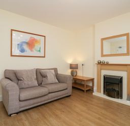 A living room with a sofa two cushions a wooden table lamp a fireplace and a mirror at 21 Eamont Park in Penrith