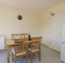 A dining area with a wooden table set for four with plates glasses and a bottle and a white fridge near a closed door at 21 Eamont Park Penrith