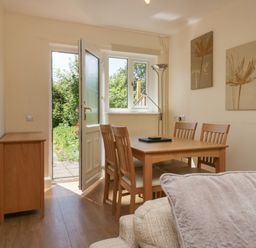 A dining area with wooden table and chairs beside an open door leading to a garden at 12 Eamont Park in Penrith