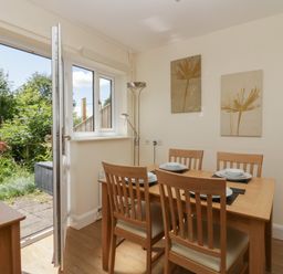 A dining room with a wooden table set for four and an open door leading to a garden at 12 Eamont Park in Penrith