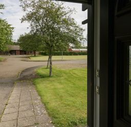 A view of a sidewalk and grassy area with trees and buildings in the background at 9 Eamont Park in Penrith