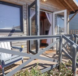A small patio with a gray wooden chair and yellow cup outside a wooden house with open glass doors at Sea Spray in Lyme Regis