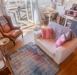 A living area with a white sofa with pink pillows a brown armchair a colorful rug a wooden floor and a small dining table near a kitchen at Sea Spray Lyme Regis