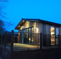 A wooden cabin with glass-railed deck and large windows at Loubi's Lakeside Lodge M1 Fallbarrow Park near Bowness-On-Windermere