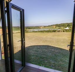 An open glass door leading to a grassy lawn with a pond and hills in the background at Ailsa Craig in Hillhampton Great Witley