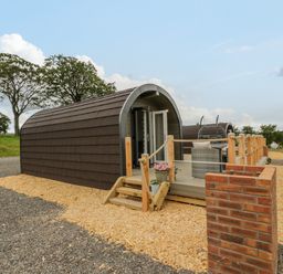 An outdoor wooden pod with a small porch and seating area surrounded by wood chips at Laird Lodge 2 in Lochmaben
