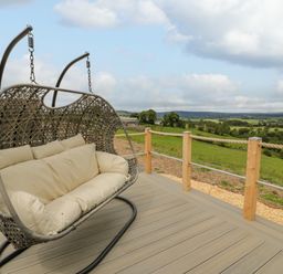 A woven hanging outdoor chair on a wooden deck overlooking green fields and hills at Laird Lodge 2 in Lochmaben