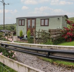 A shepherd's hut with flowers and a fence at The Herdsman Luxury Shepherds Hut in Barnoldswick