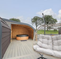 An outdoor area with a cushioned hanging chair and a covered hot tub at Laird Lodge 3 in Lochmaben