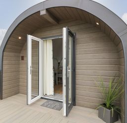 The entrance of a pod-style building with double glass doors open to the inside with a plant in a square pot on the right at Laird Lodge 3 in Lochmaben