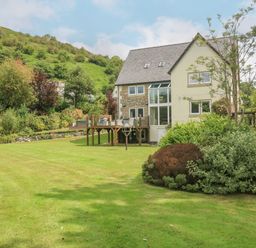 A house with a wooden deck overlooking a large lawn and garden on a hillside at Tan Yr Allt in Dolanog near Meifod Powys