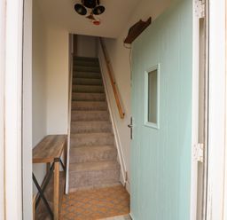 An entrance hallway with carpeted stairs a wooden bench and a light blue front door at Jolly Sailors Retreat - Wells next the Sea in Wells-Next-The-Sea