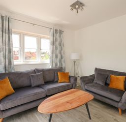 A living room with two grey sofas with orange and grey cushions a wooden coffee table and patterned curtains at Jolly Sailors Retreat - Wells next the Sea