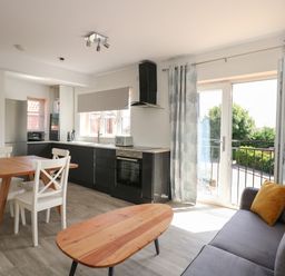 A kitchen and dining area with a wooden table and white chairs next to a gray sofa and coffee table at Jolly Sailors Retreat - Wells next the Sea in Wells-Next-The-Sea