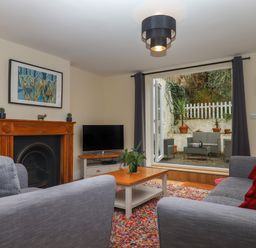 A living room with gray sofas a coffee table a fireplace and a television with an open door to a patio outside at Mimosa in Dawlish