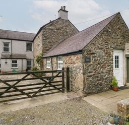 A stone cottage with a wooden gate and paved area at Ty Gwenyn in Rhydwyn