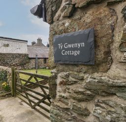 A stone wall with a sign that says Ty Gwenyn Cottage and a wooden gate leading to a garden at Ty Gwenyn in Rhydwyn