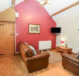 A living room with two brown leather sofas a wooden door a TV mounted on a red wall a wooden coffee table and framed pictures at Ty Gwenyn in Rhydwyn