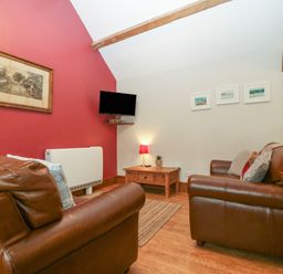 A living room with brown leather sofas a wooden coffee table a small lamp and a wall mounted television at Ty Gwenyn in Rhydwyn