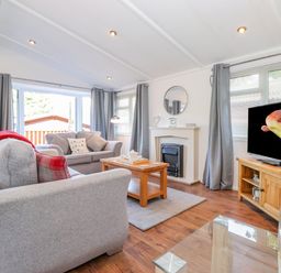 A living room with gray sofas a wooden coffee table a fireplace a television and large windows at Fell Foot Lodge Fellside 9 Limefitt Park near Troutbeck