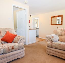 A living room with two floral patterned sofas and an orange cushion with a mirror on the wall at Little Rowan at Rowan Park Farm in Ashwater