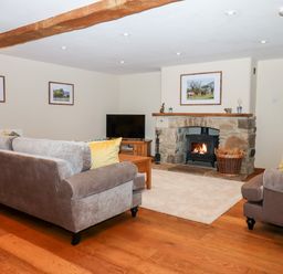 A living room with sofas a stone fireplace with a wood burning stove a television and wooden flooring at Little Orchard in Ashburton Down near Ashburton