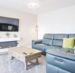 A living room with a gray leather sofa with green pillows a wooden coffee table wall mounted television and a modern fireplace at Aelfor in Harlech