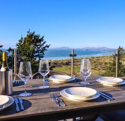 An outdoor dining table set with plates wine glasses cutlery and a bottle of wine overlooking a coastal landscape at Aelfor in Harlech