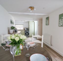 A dining table set with plates glasses and a vase of flowers in a room with a kitchen in the background at 2 Penporth in Rhayader