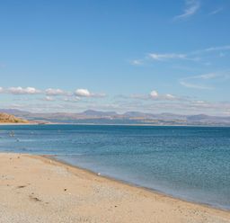 A sandy beach with calm blue water and distant hills under a blue sky at Moondunes - Pwllheli in Chwilog