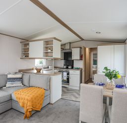 A living room with a gray sectional sofa a dining table with four chairs and a kitchen area at Moondunes - Pwllheli in Chwilog