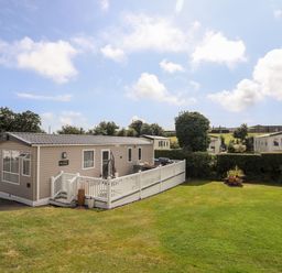 A caravan with a white fenced deck on a grassy plot under a partly cloudy sky at Moondunes - Pwllheli in Chwilog