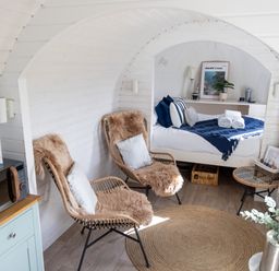 A small room with two wicker chairs with cushions a bed with blue and white bedding a round woven rug and a microwave on a cabinet at Andrus - Mayflower Meadow in Brandesburton