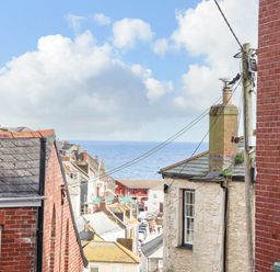A view of rooftops and buildings overlooking the sea with a partly cloudy sky at Chy An Mor in Mevagissey