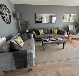 A living room with two sofas, a coffee table, a lounge chair, plants, wall clock, and framed pictures at Old Orchard in Saundersfoot