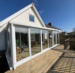 A deck with wooden railings outside a house with large glass sliding doors and a pitched roof at Old Orchard in Saundersfoot