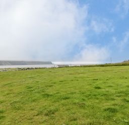 A grassy field with houses at a distance under a cloudy sky at 13 Trawmore Cottages in Keel County Mayo