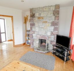 A living room with a stone fireplace a TV on a stand a grey rug and red curtains at 13 Trawmore Cottages Keel County Mayo